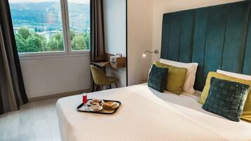 Ein Hotelzimmer mit Bett, Schreibtisch und Fenster mit Blick auf Grünflächen.