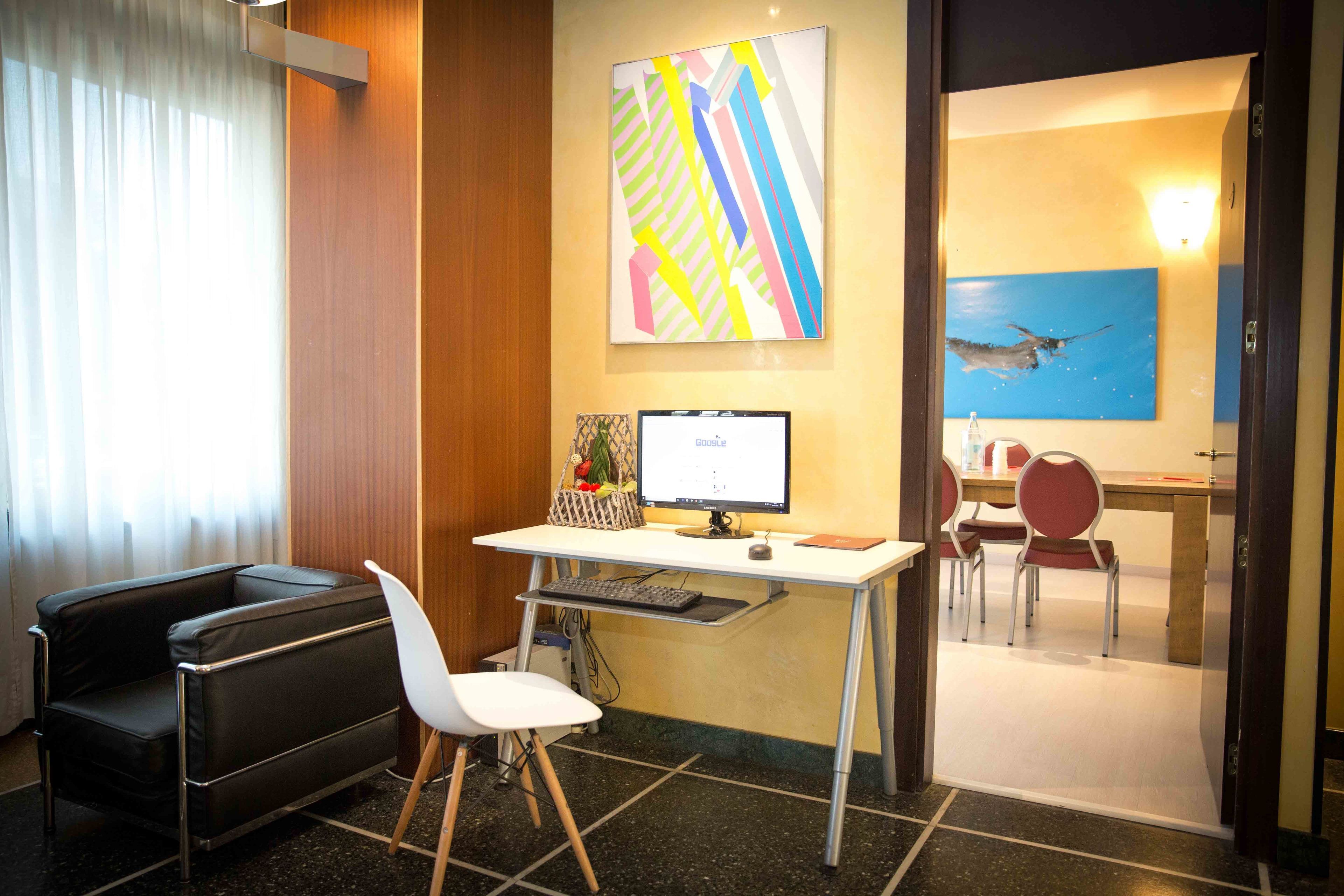 Ein modernes Hotelzimmer mit Schreibtisch, Computer, schwarzem Ledersofa und weißem Sessel.