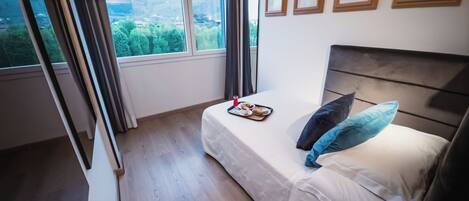 A bedroom with a bed, a tray with breakfast items, a window with a view of greenery, and framed pictures on the wall.