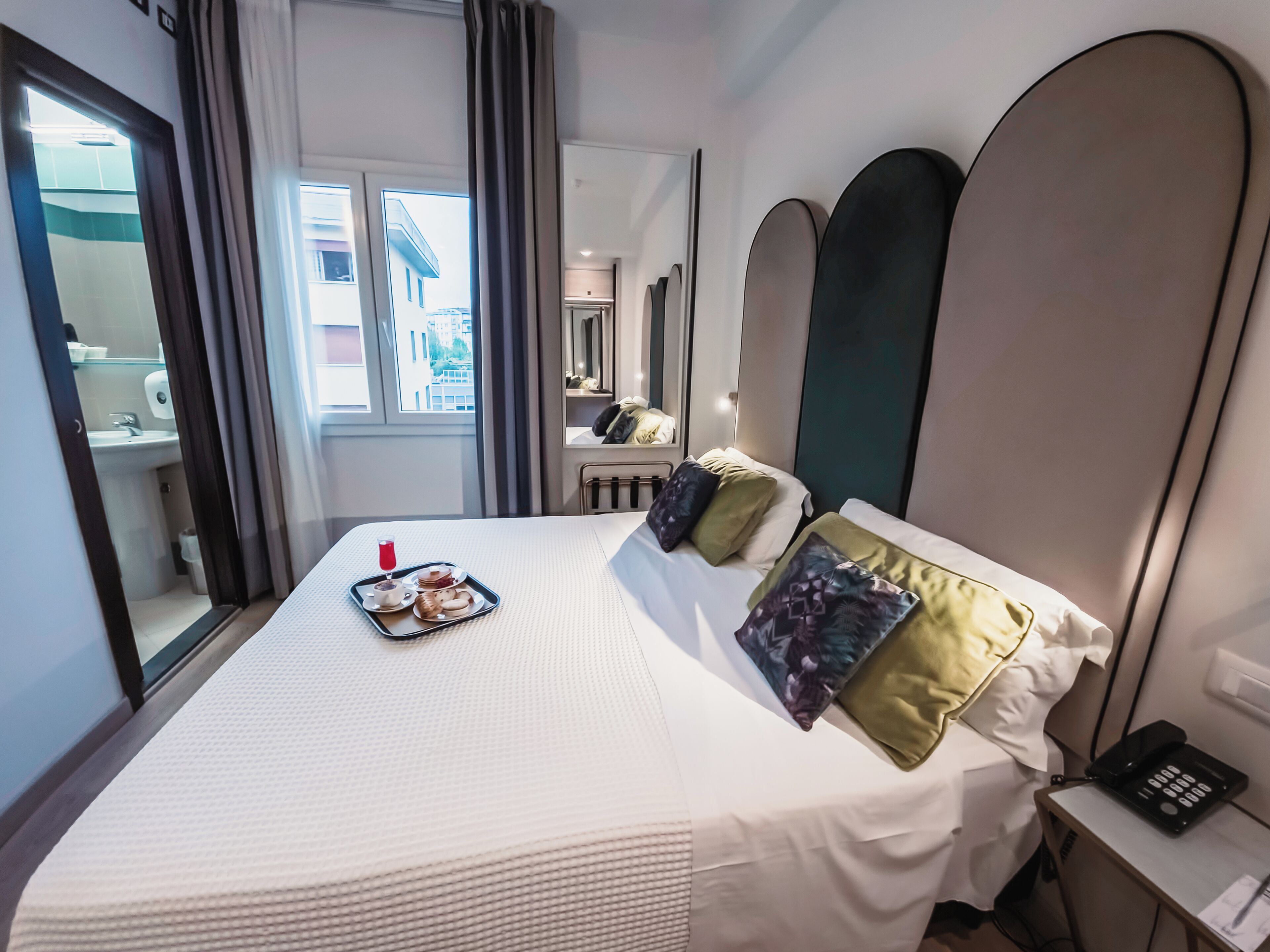 A hotel room with a large bed, a bedside table with a phone, and a window with curtains.