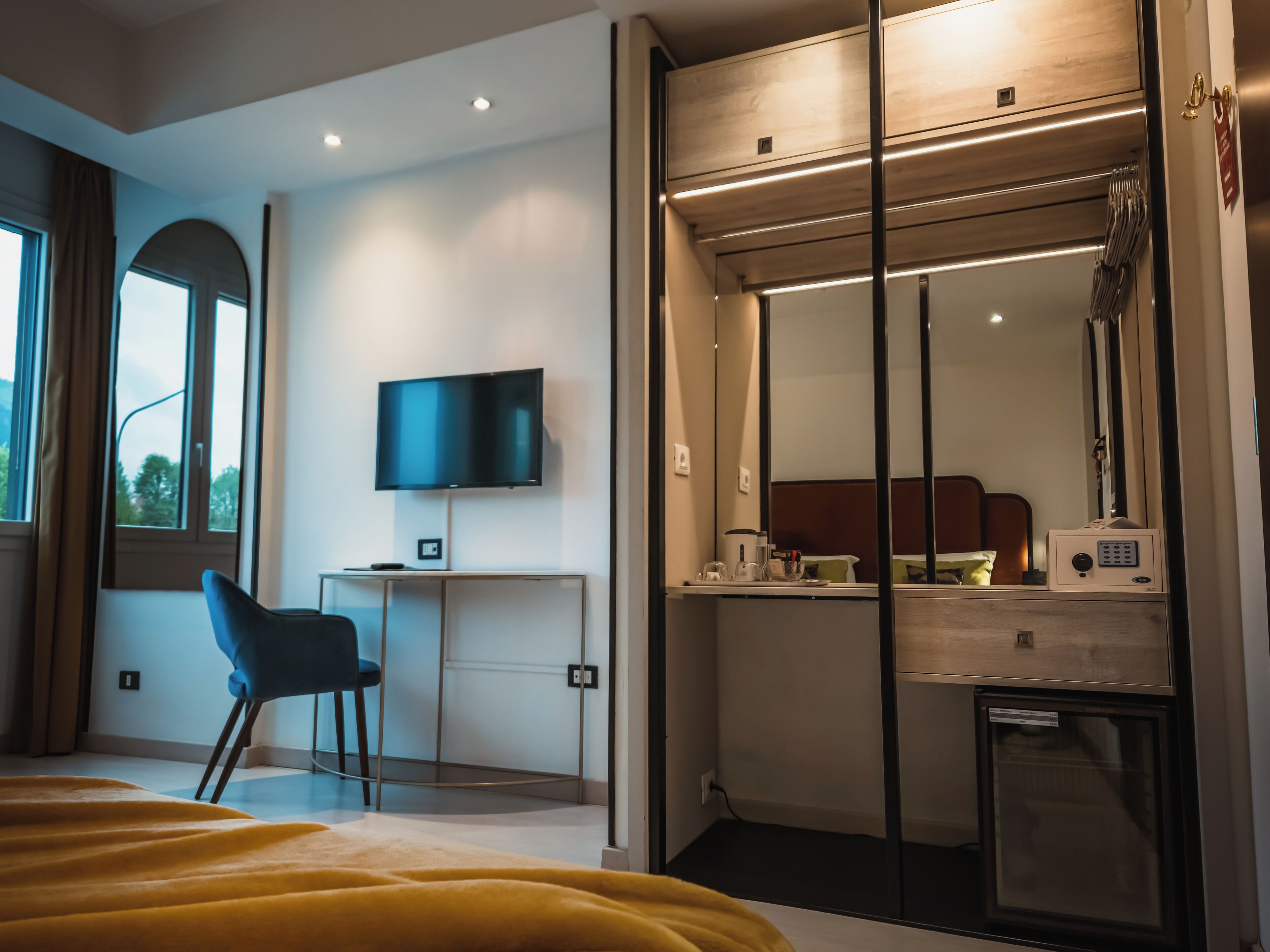 Een moderne hotelkamer met een bed, een bureau met een computer, een televisie en een minibar.
