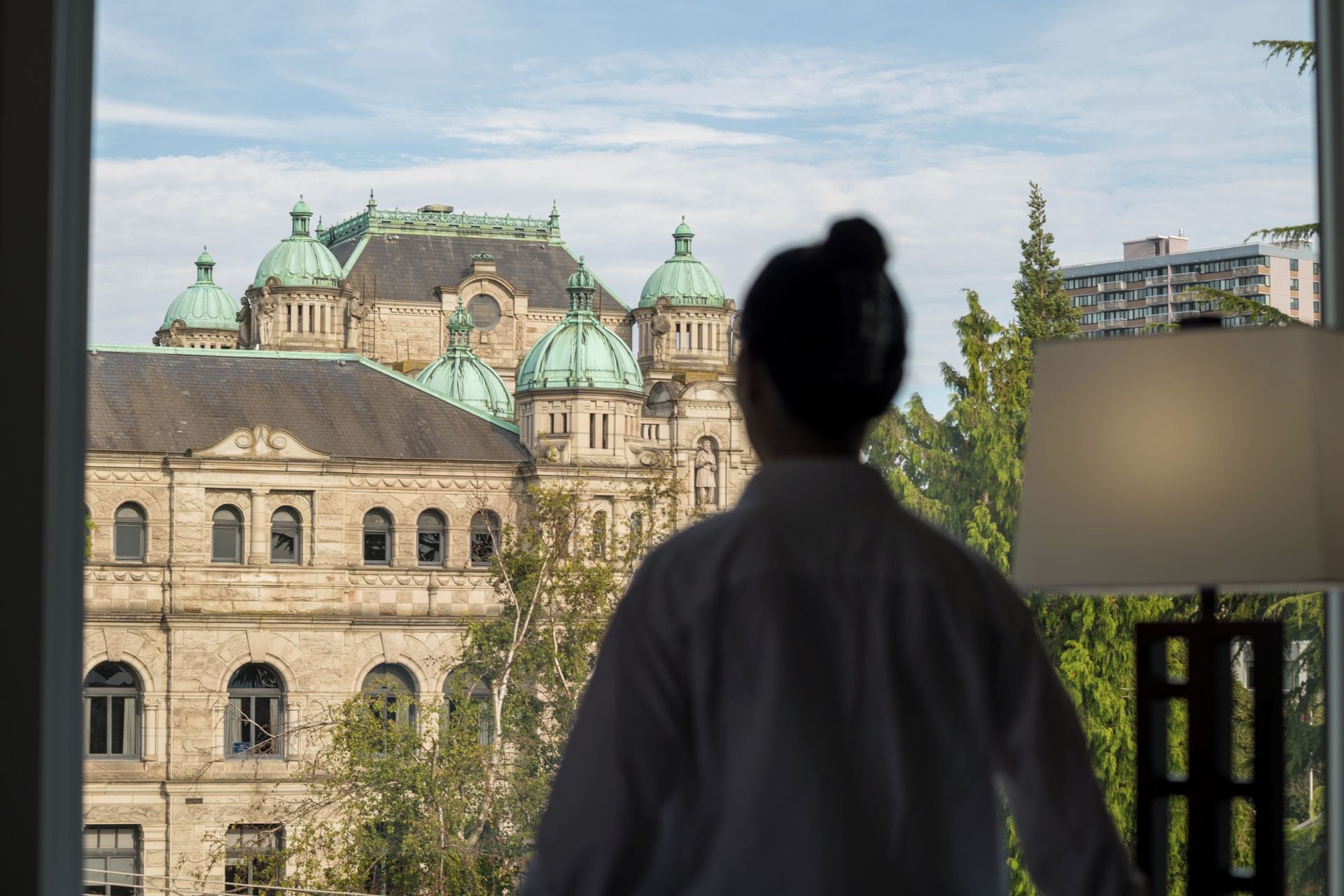Une personne se tient à l’intérieur d’un bâtiment et regarde un édifice historique doté de plusieurs dômes et présentant un style architectural classique.