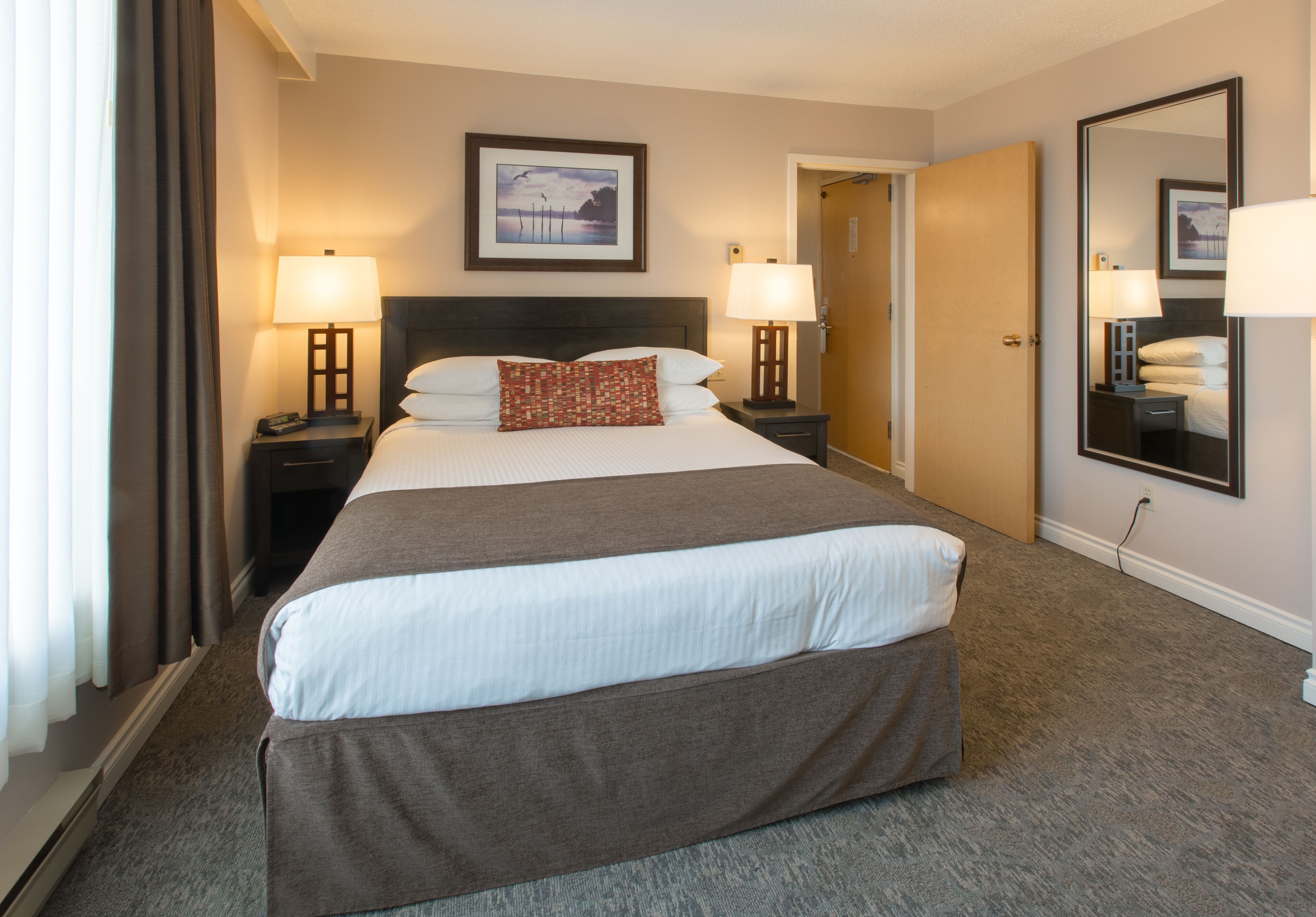 A hotel room with a large bed, two bedside tables with lamps, a framed picture on the wall, and a mirror.
