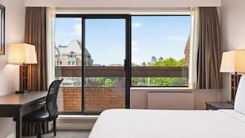 Habitación de hotel con cama, escritorio, silla y ventanas amplias con vista a la ciudad.