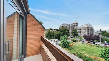 A balcony with a view of a large building complex, a parking area, and a grassy landscape.