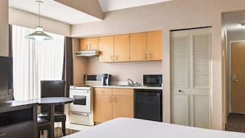 Een compacte hotelkamer met een kitchenette, een bed, een bureau met stoel en een televisie.