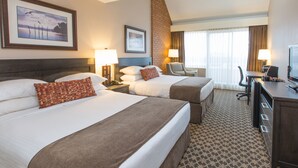 A hotel room with two beds, a desk, a TV, and a window with curtains.