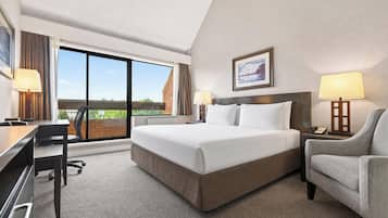 A hotel room with a large bed, a desk, a chair, a window with curtains, and a framed picture on the wall.