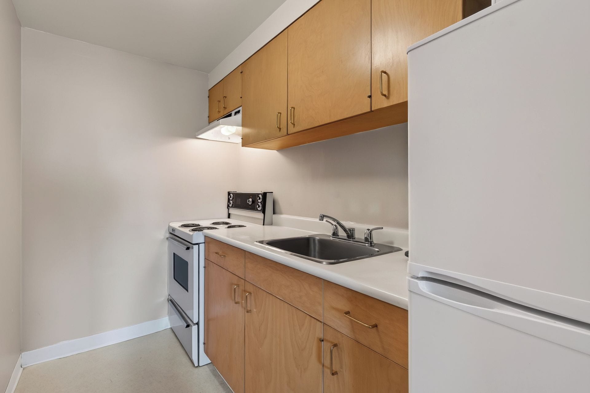 A compact kitchen with white cabinets, a stove, a sink, and a refrigerator.