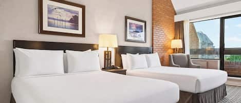 Habitación de hotel con dos camas, una pared de ladrillo decorativa y un ventanal con vistas.