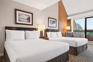 A hotel room with two beds, a brick accent wall, and a large window offering a view.