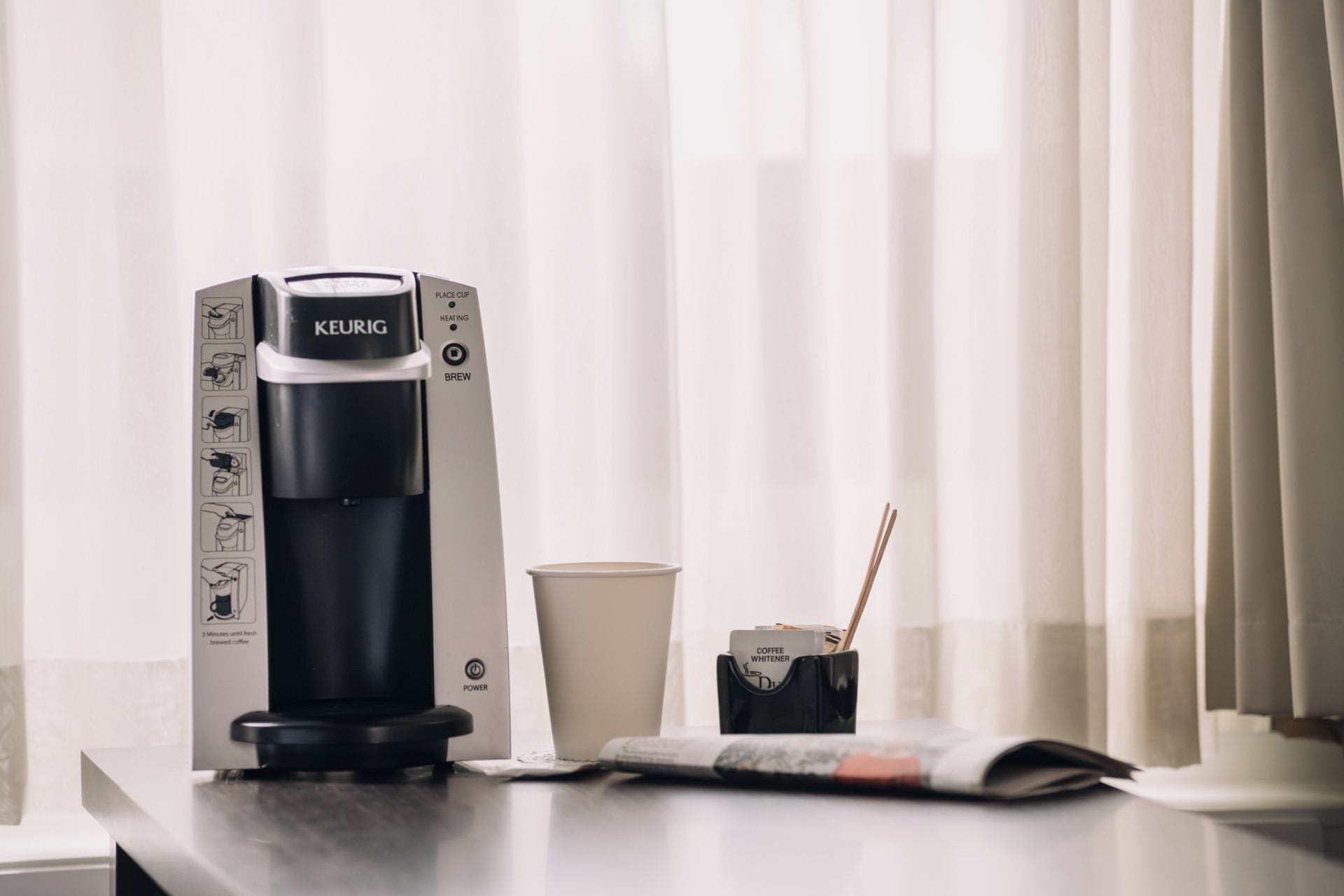 A Keurig coffee maker on a countertop with a cup of coffee and a coffee whitener.