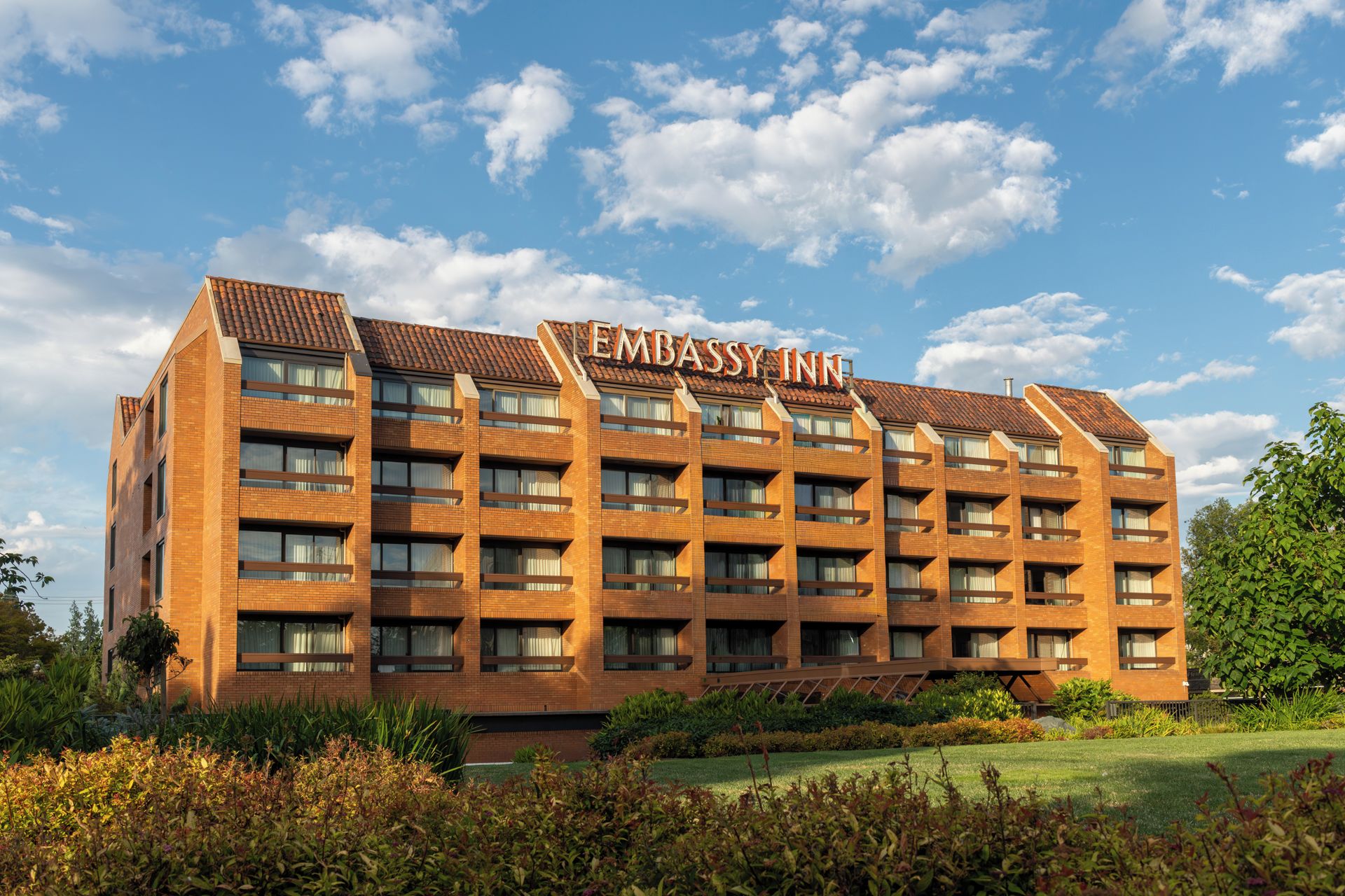 A multi-story building with the sign 'Embassy Inn' on the roof, surrounded by greenery and a clear sky.