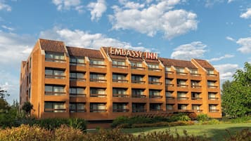 A multi-story building with the sign 'Embassy Inn' on the roof, surrounded by greenery and a clear sky.