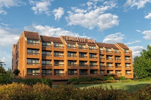 Een meerlaags gebouw met de naam 'Embassy Inn' op het dak, omgeven door groen en een heldere lucht.