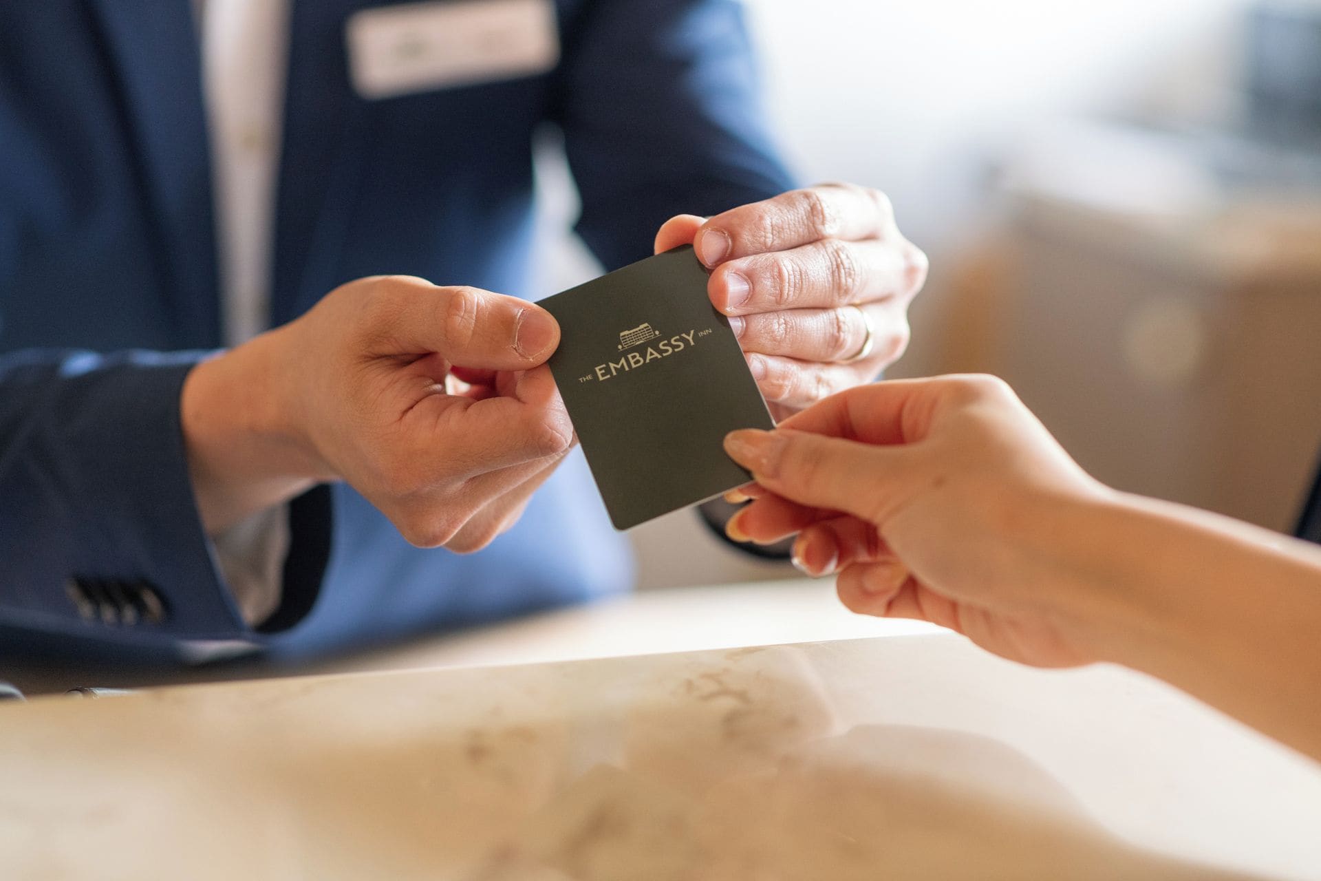 A person handing over a black card with 'THE EMBASSY' text to another individual.