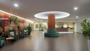 Eine geräumige Lobby mit einer zentralen Säule, Sitzgelegenheiten, einer Rezeption und Kunstwerken an den Wänden.