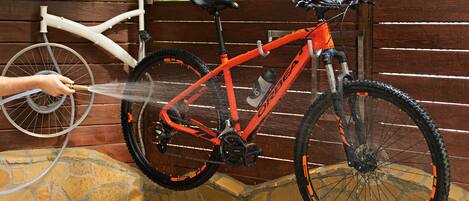 A bicycle being washed by a hose against a wooden fence.