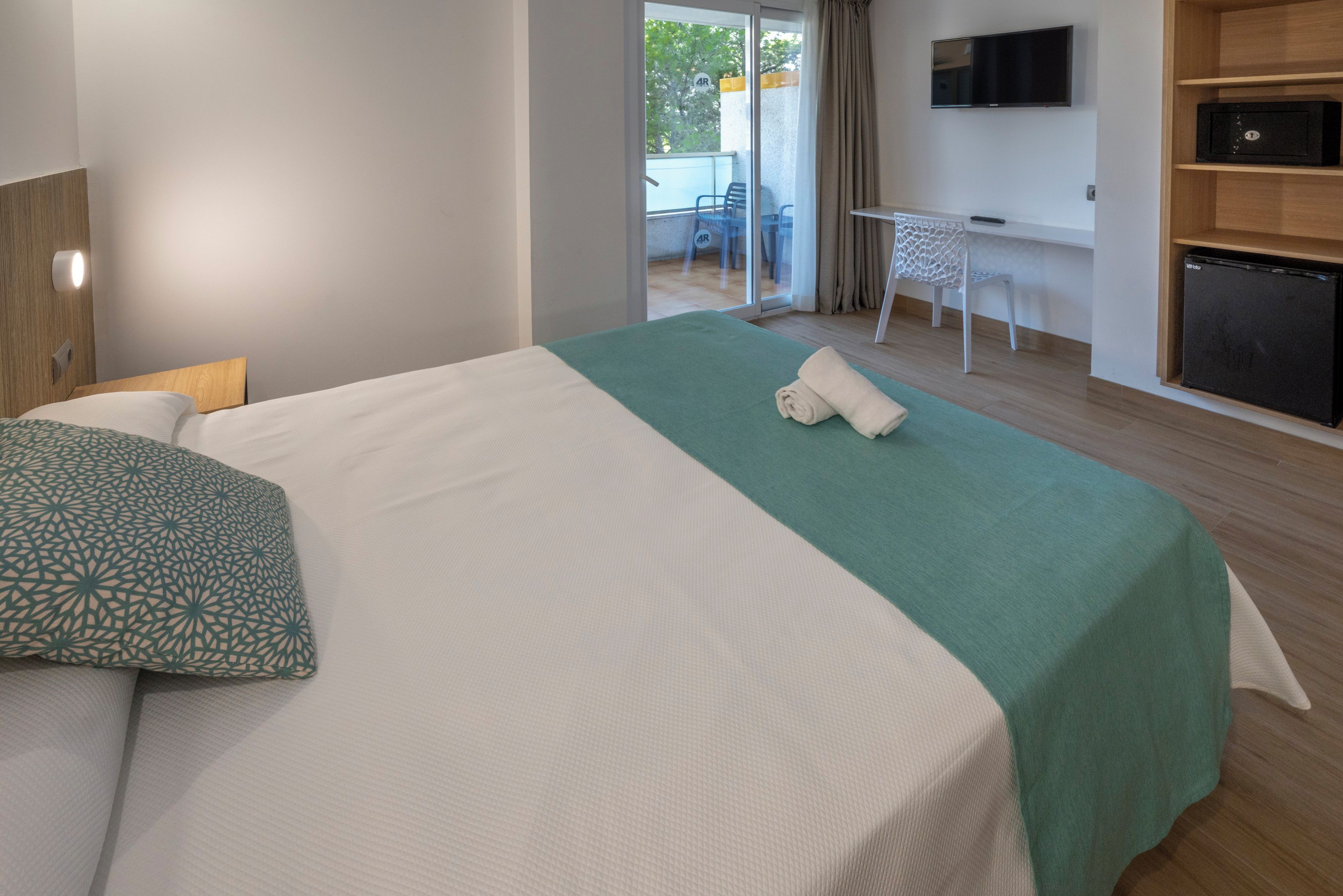 A hotel room with a bed, a desk, a TV, and a view of the outside.
