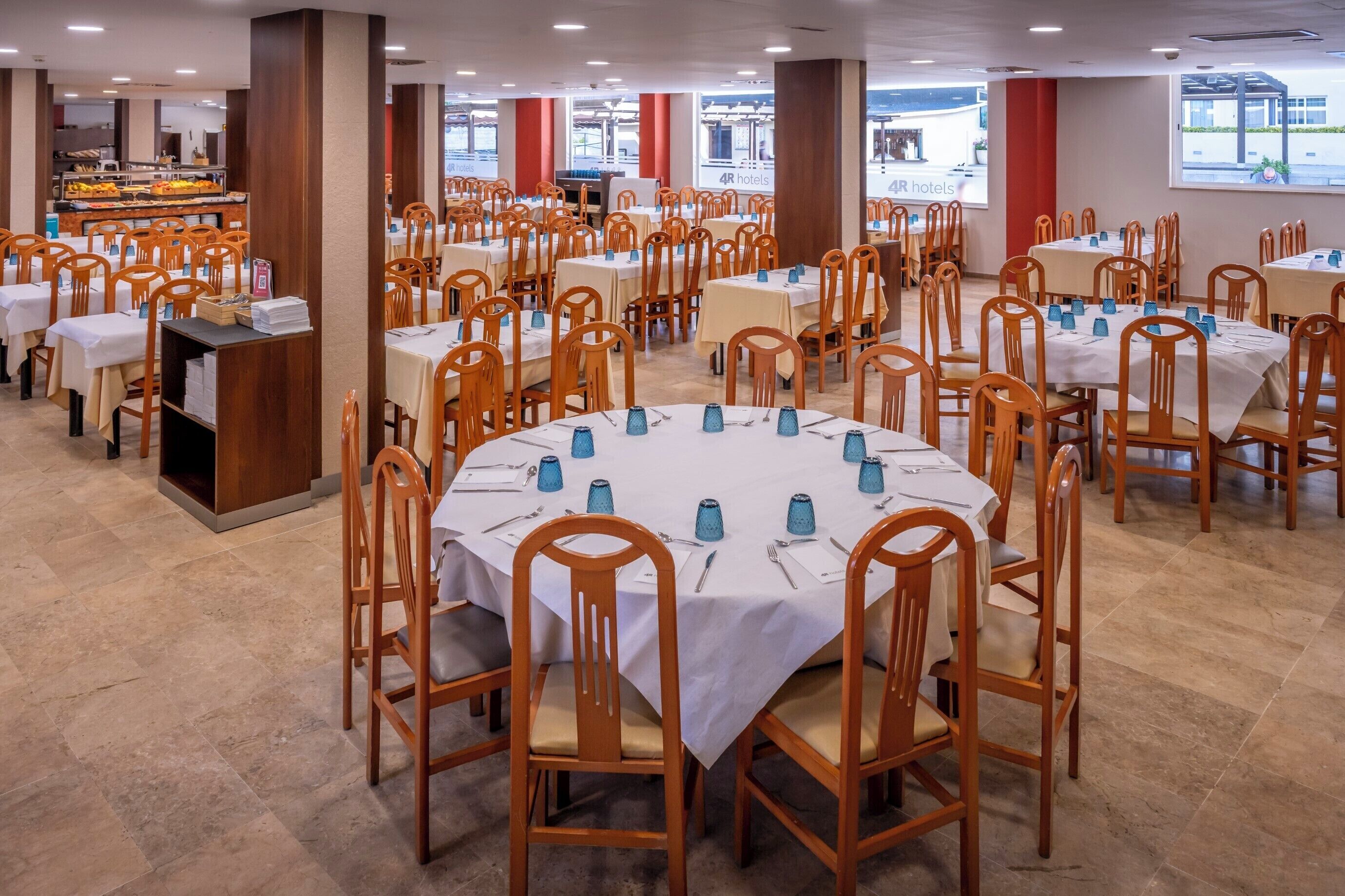 Un comedor amplio con varias mesas redondas, cada una con sillas y vasos azules.