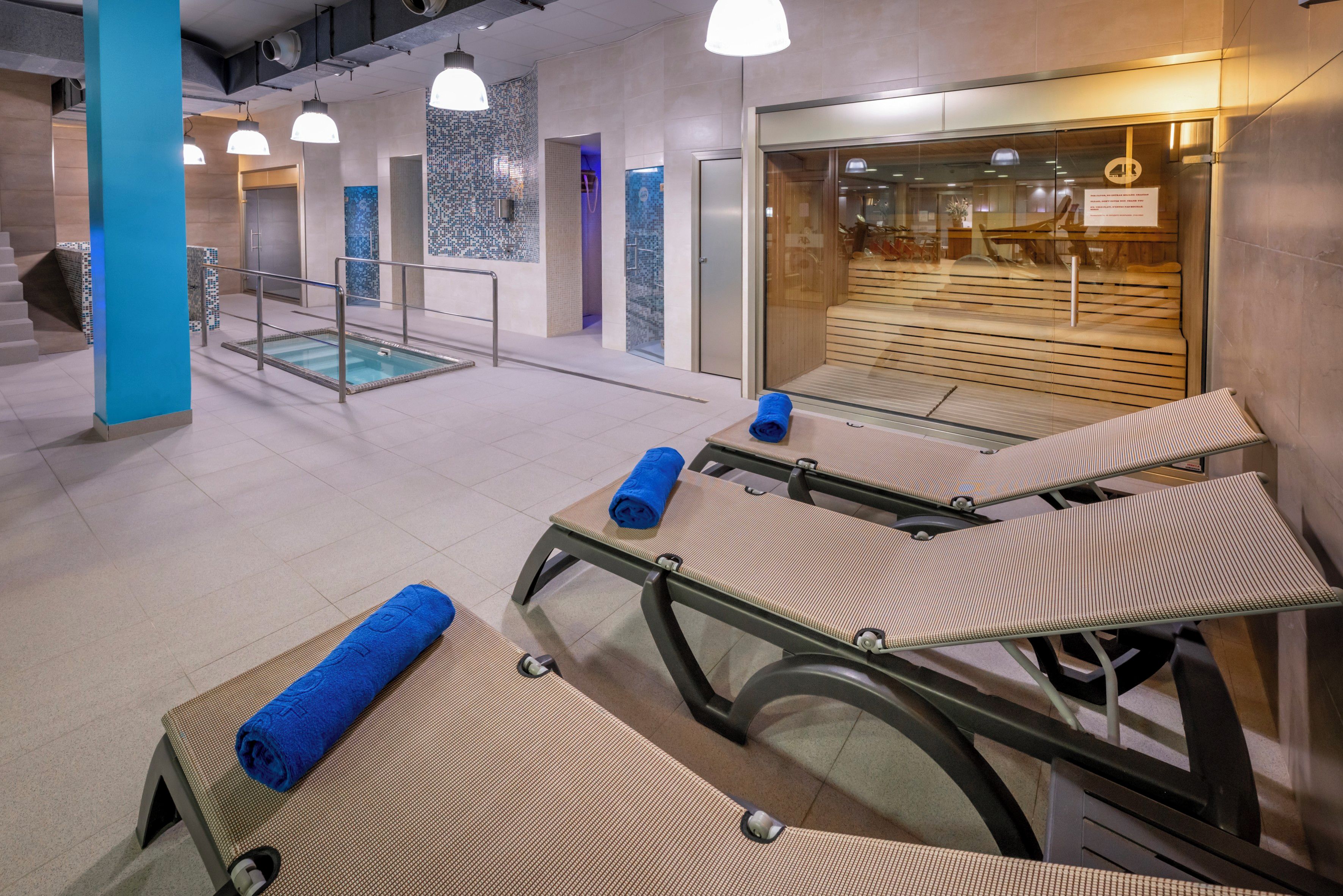 Un área de spa moderna con camillas de masaje, toallas y una sala de relajación con paredes de vidrio.