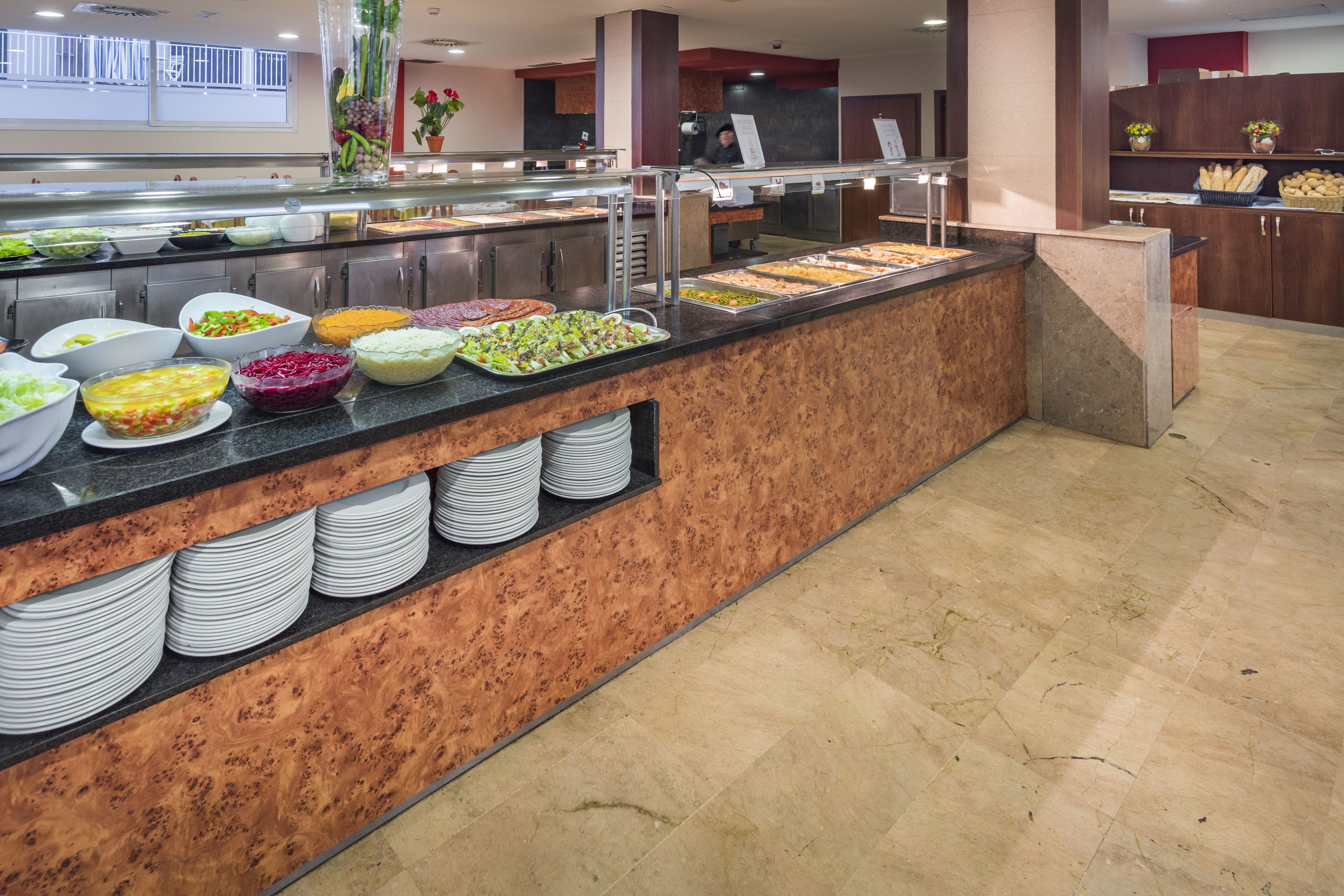 A buffet with various food items and stacked white plates.