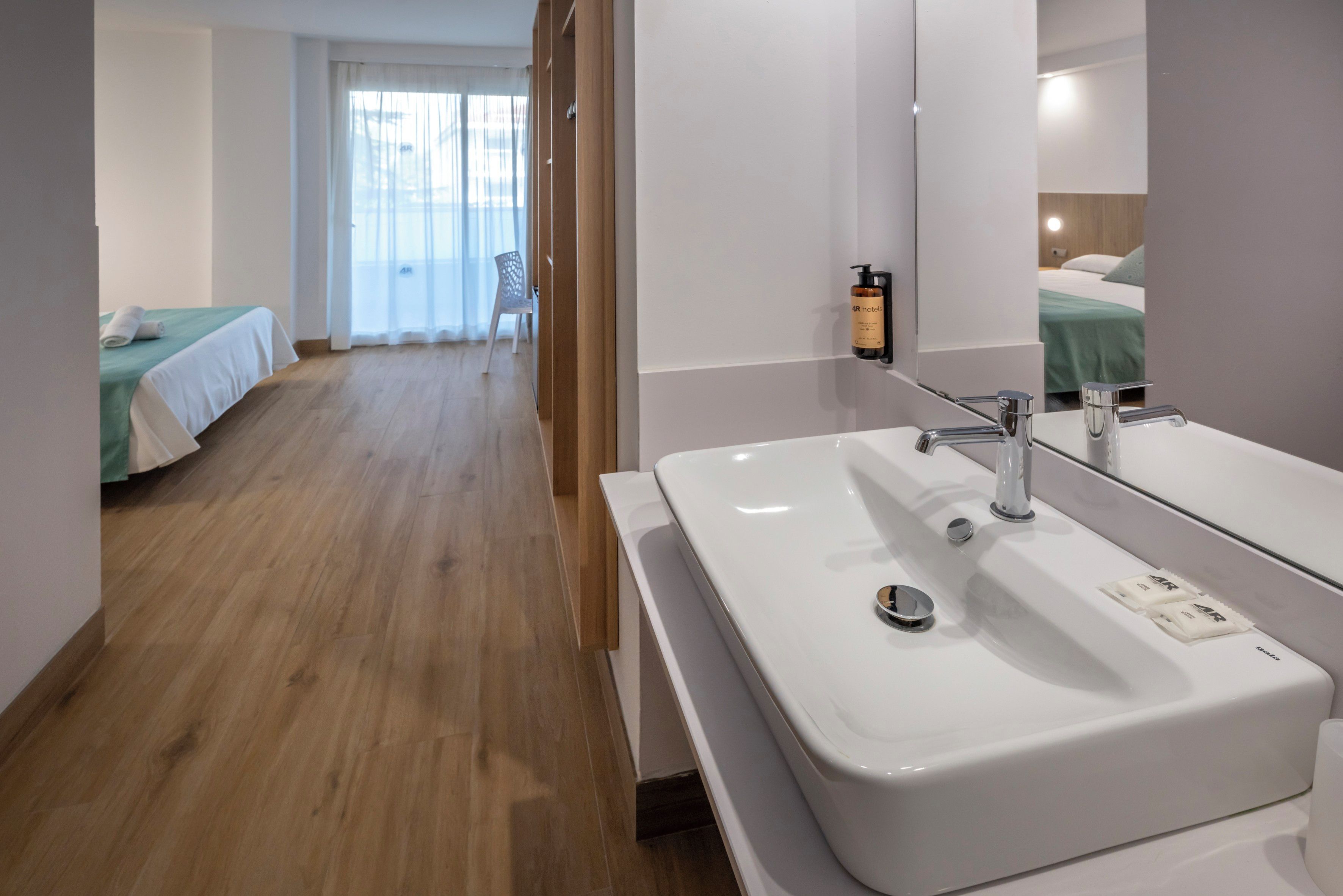Habitación de hotel con un lavamanos grande en el baño, un espejo y una cama con cubrecama verde.