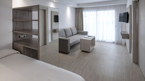 Ein modernes Hotelzimmer mit einem großen Bett, einer Couch, einem Couchtisch, einem an der Wand befestigten Fernseher und einem großen Fenster mit Vorhängen.