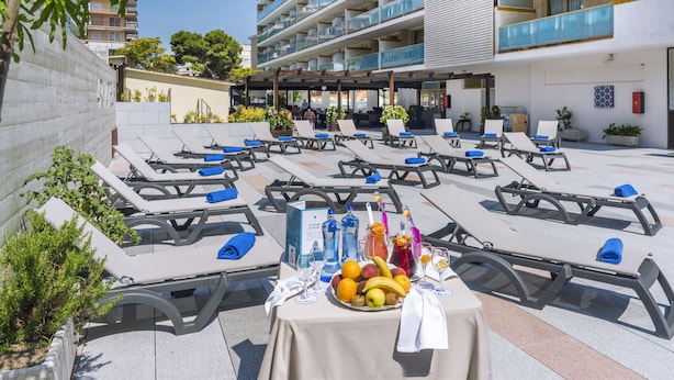 Eine Dachterrasse mit Liegestühlen, einem Tisch mit Obst und Getränken und Blick auf die Balkone des Gebäudes.