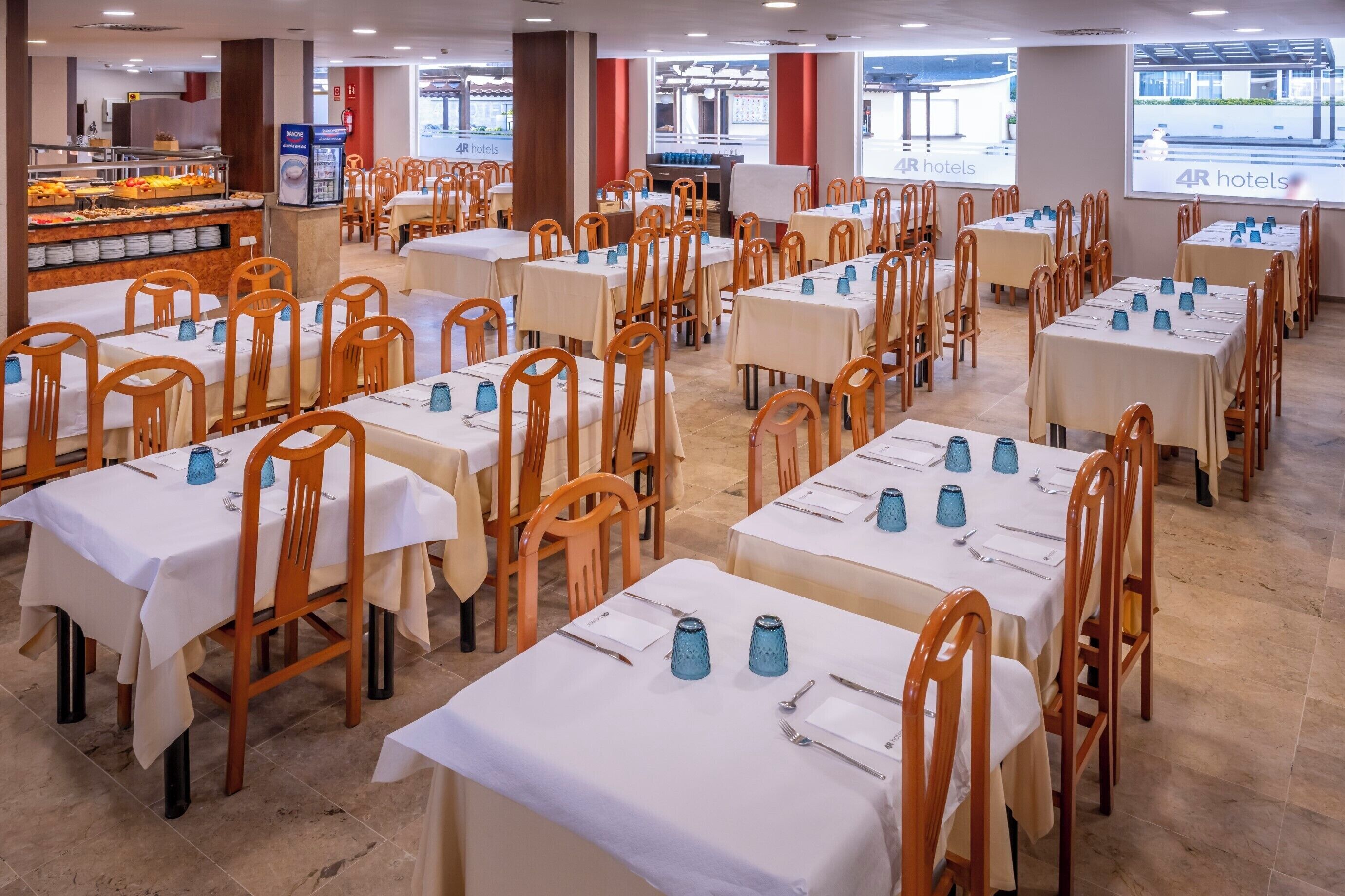 Een eetgedeelte met meerdere tafels en stoelen, een buffet met diverse gerechten, en een scherm waarop de naam van het hotel wordt geprojecteerd.