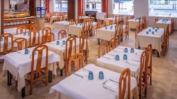 Een eetgedeelte met meerdere tafels en stoelen, een buffet met diverse gerechten, en een scherm waarop de naam van het hotel wordt geprojecteerd.