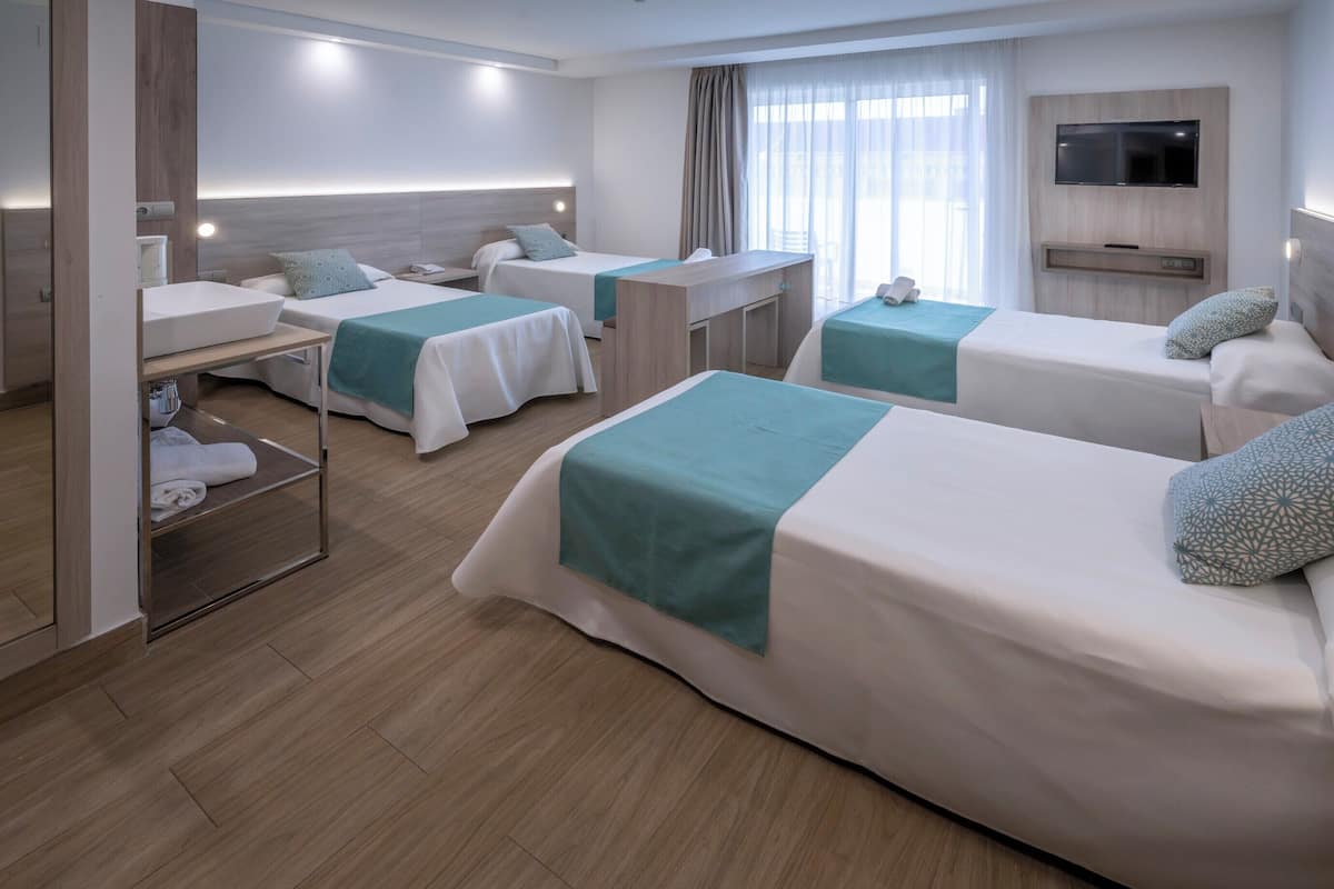 A hotel room with two beds, a desk, a TV, and a window with curtains.