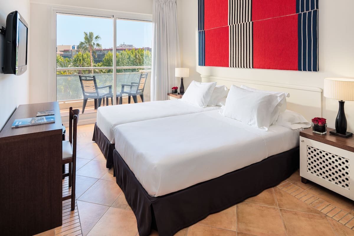 A hotel room with a large bed, a desk, and a balcony with chairs.