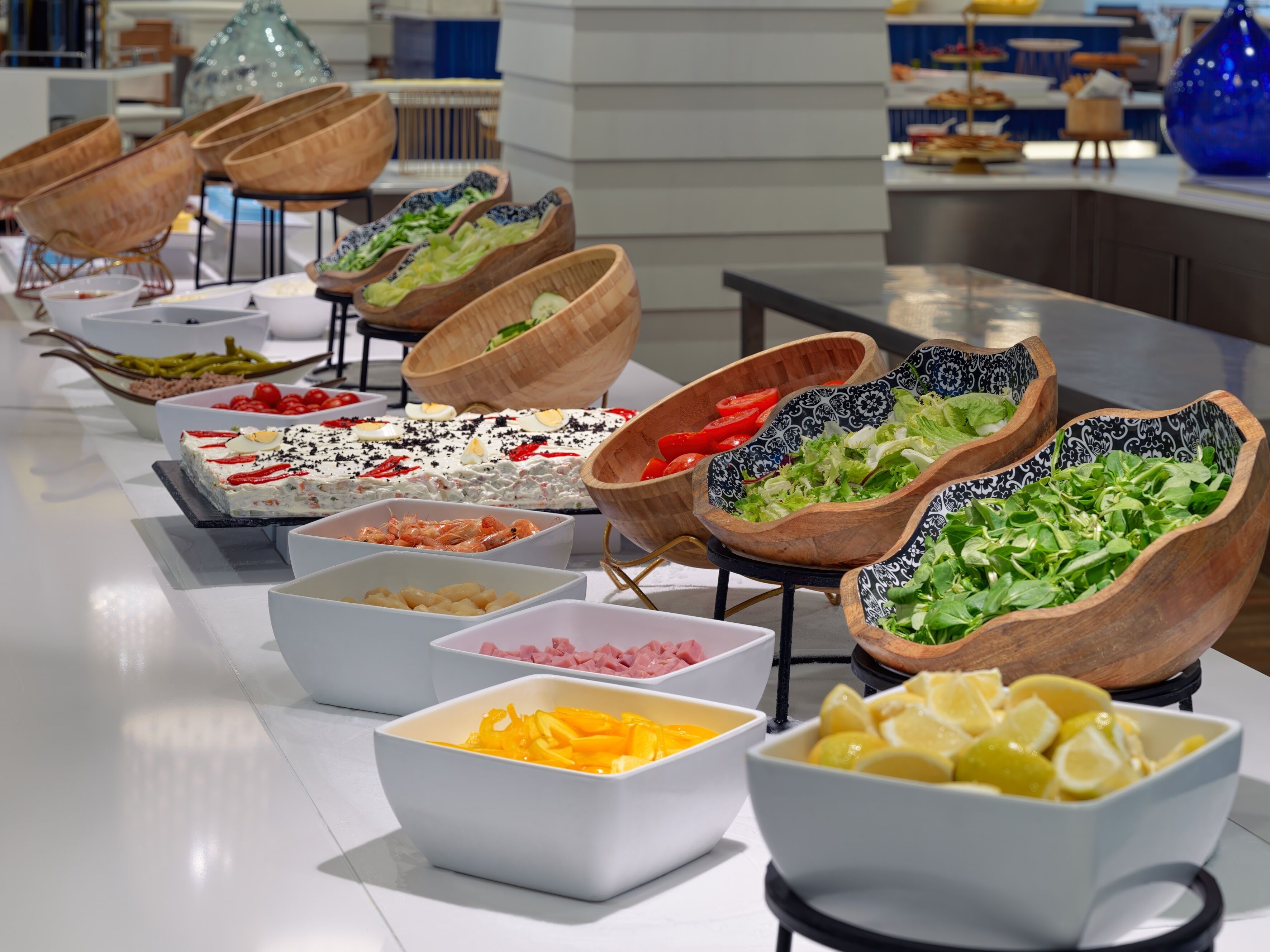 Un bufé con diversos alimentos en cuencos y bandejas, como ensaladas, frutas y carnes.