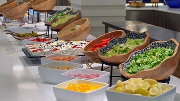 Un bufé con diversos alimentos en cuencos y bandejas, como ensaladas, frutas y carnes.