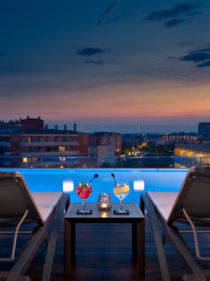 Un área de descanso junto a la piscina con dos sillas, una mesa, dos bebidas y una vela.