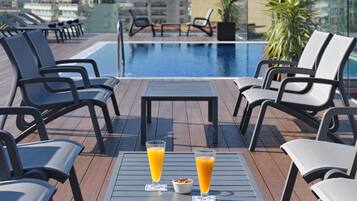 A rooftop pool area with lounge chairs, a table with two glasses of orange juice, and a view of the city skyline.