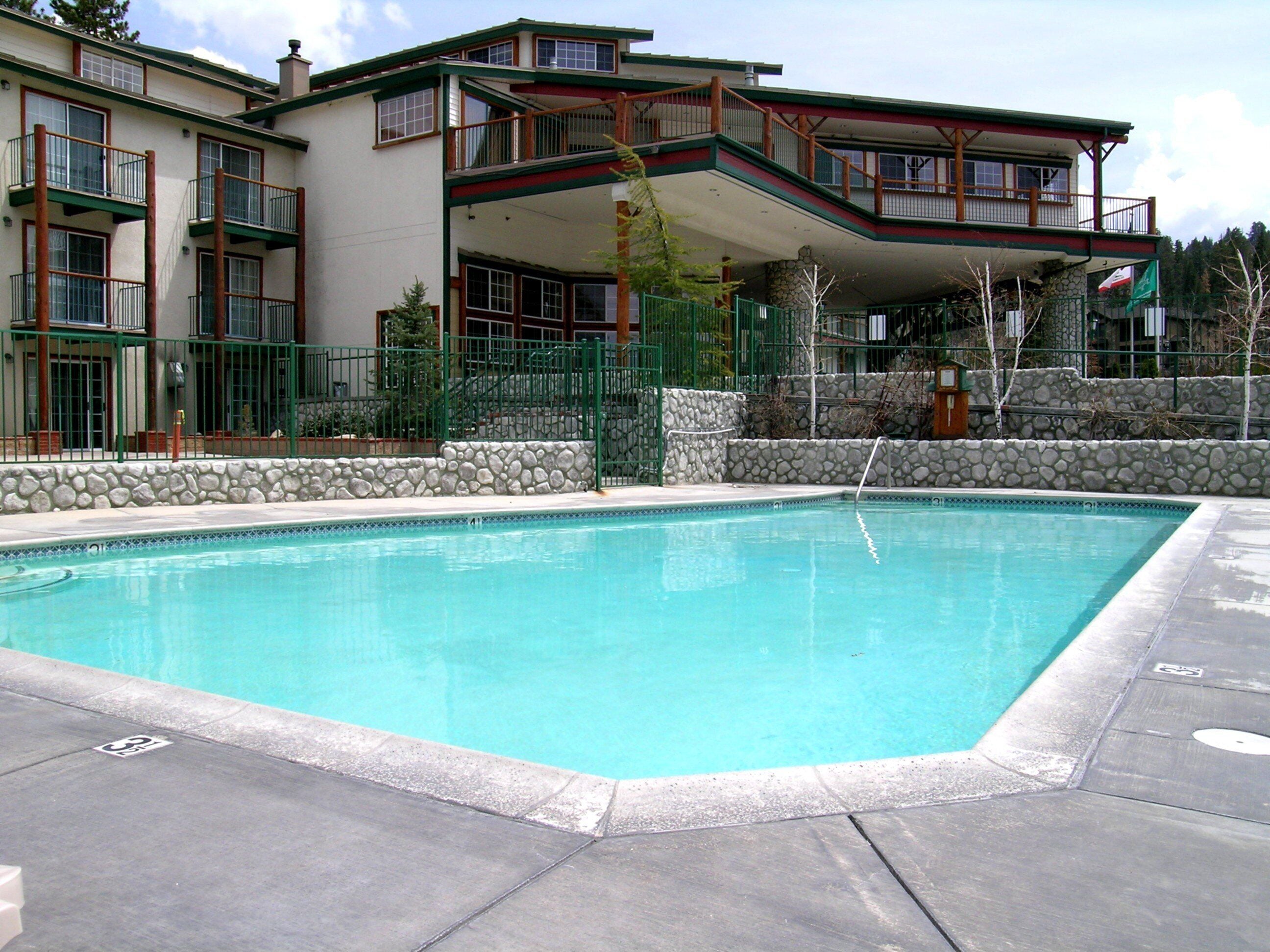 A rectangular swimming pool with a stone border, surrounded by a paved deck.