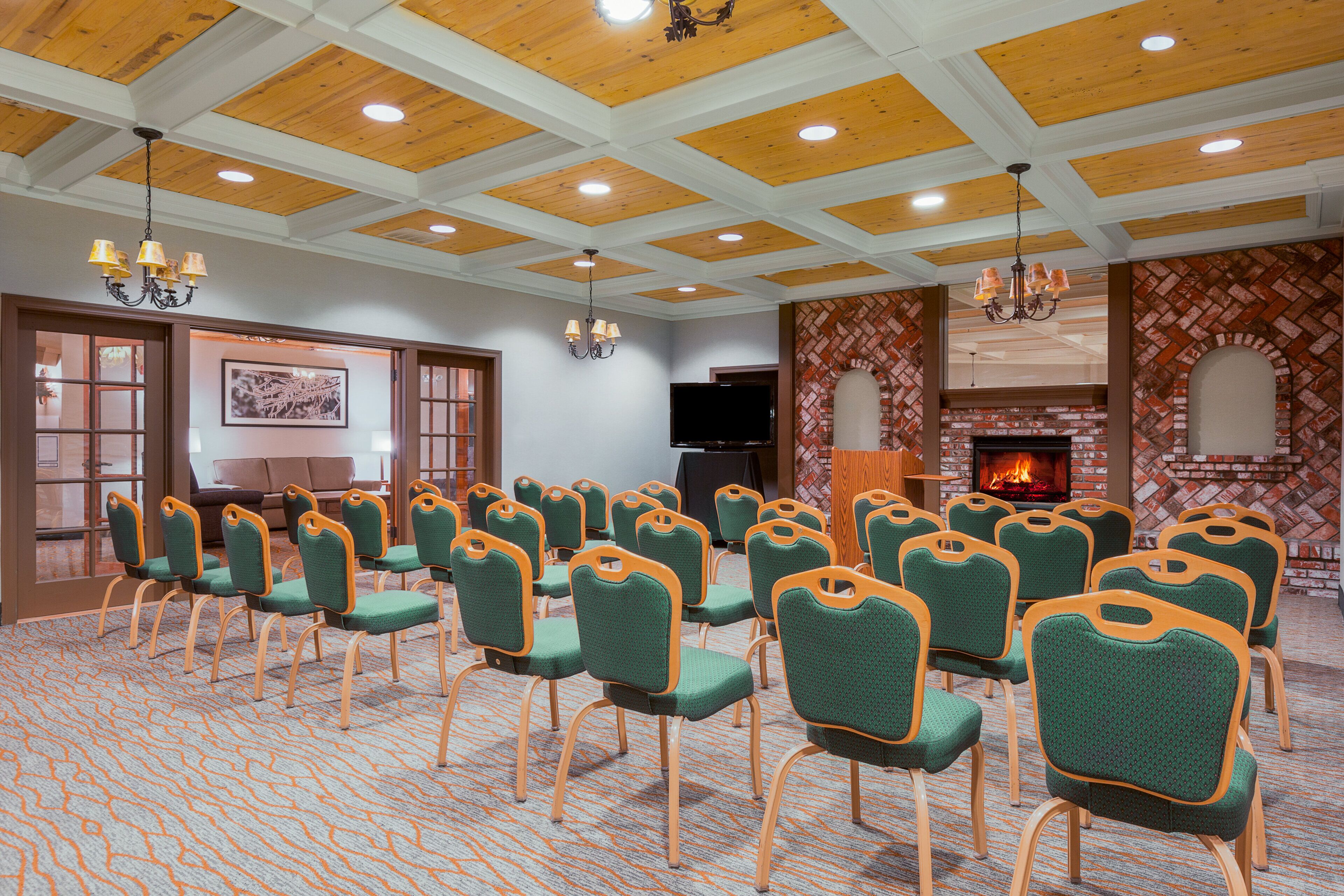A conference room with rows of green chairs, a fireplace, and a wooden ceiling.