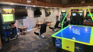 Experience the ultimate gaming haven with a retro setup featuring a pinball machine, arcade games, and a large TV.