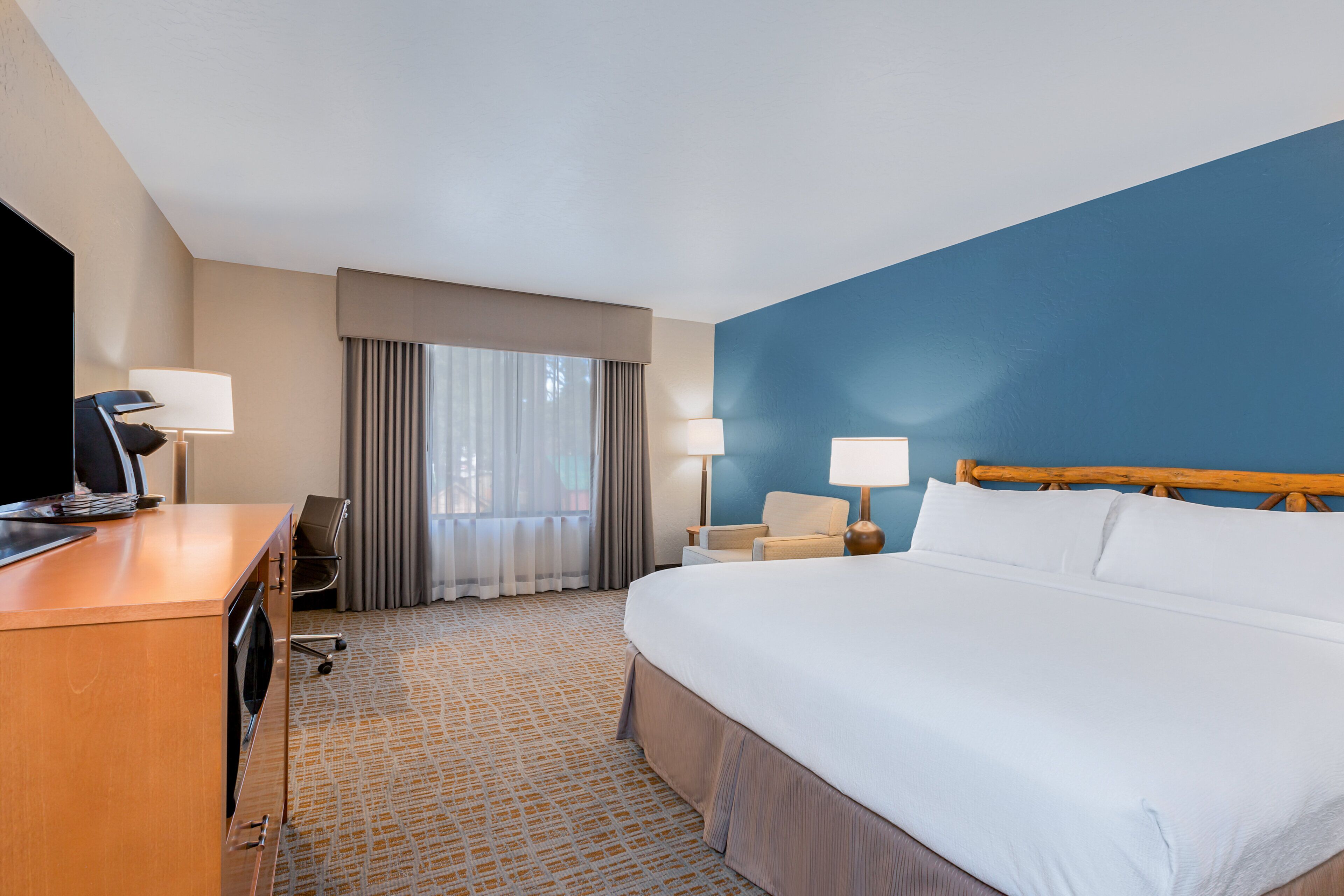 A hotel room with a large bed, a desk with a computer, a chair, and two lamps.