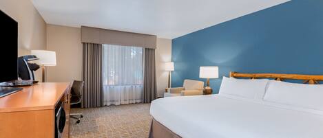 A hotel room with a large bed, a desk with a computer, a chair, and two lamps.