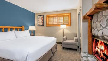 A hotel room with a bed, a chair, a fireplace, and a window with blinds.