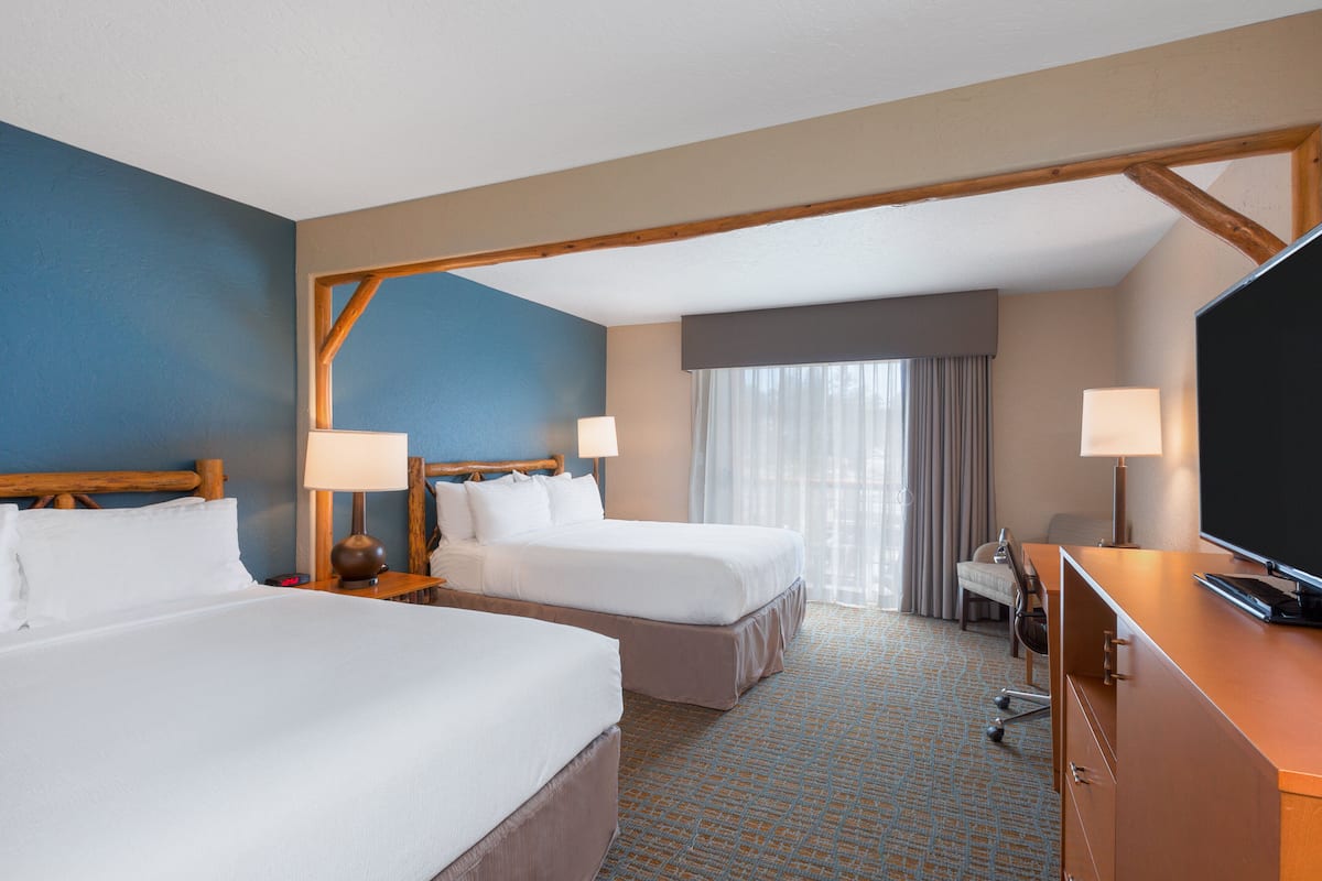 A hotel room with two beds, a desk, a television, and a window with curtains.