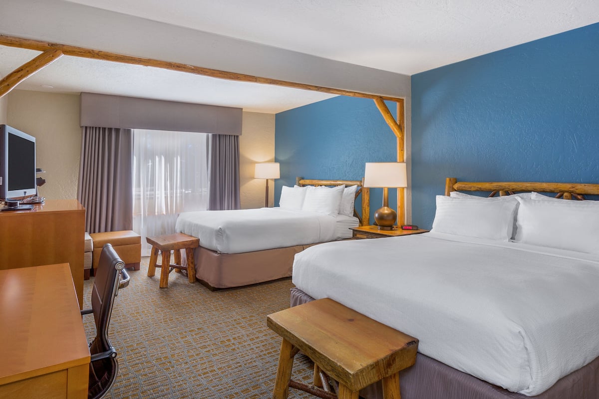 A hotel room with two beds, a desk, a chair, and a TV.