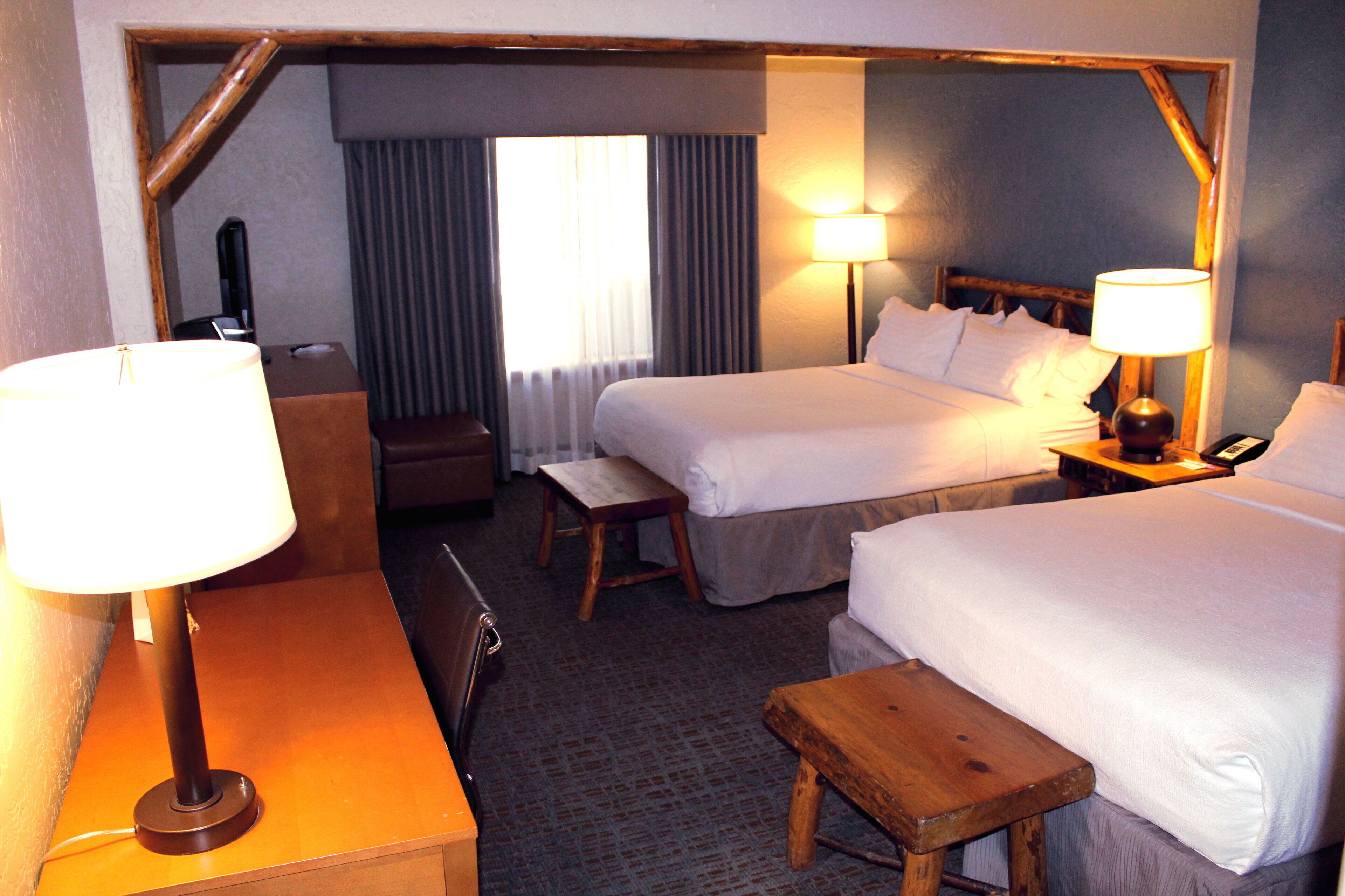Ett hotellrum med två sängar, ett skrivbord, en stol, ett litet bord och två lampor.