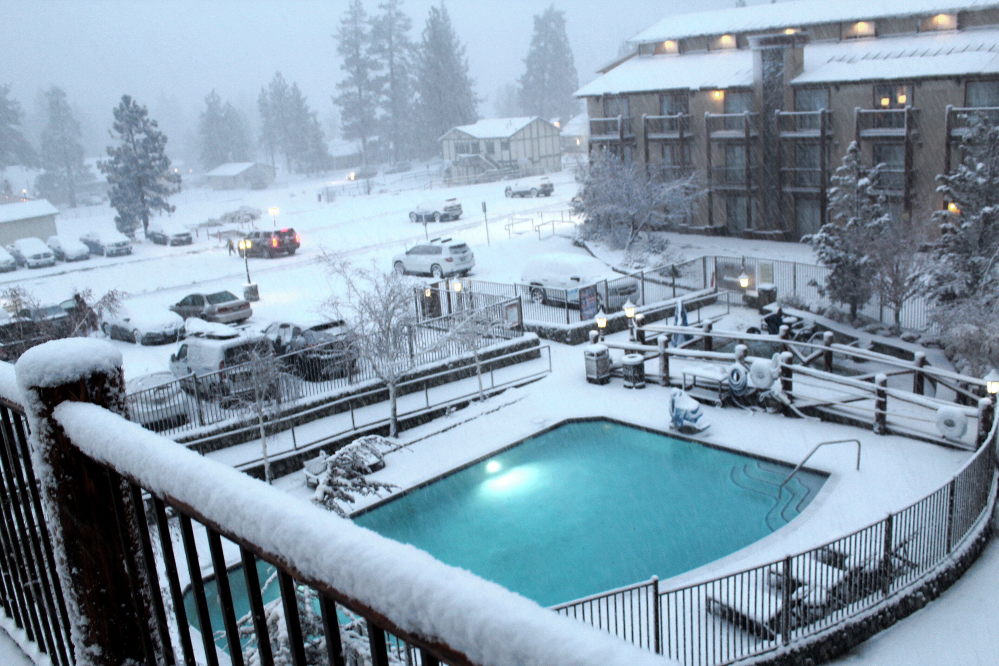 A snow-covered outdoor pool area with a pool, lounge chairs, and a building in the background.