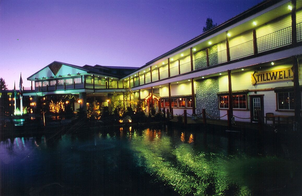 Un hotel frente al agua con piscina reflectante, varias plantas y un llamativo letrero 'Tillwell'.