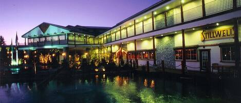 Un hotel frente al agua con piscina reflectante, varias plantas y un llamativo letrero 'Tillwell'.