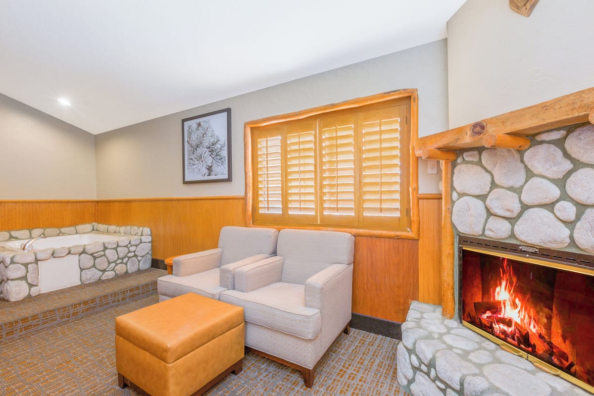 A room with a stone fireplace, a sofa, a bench, and a bathtub.